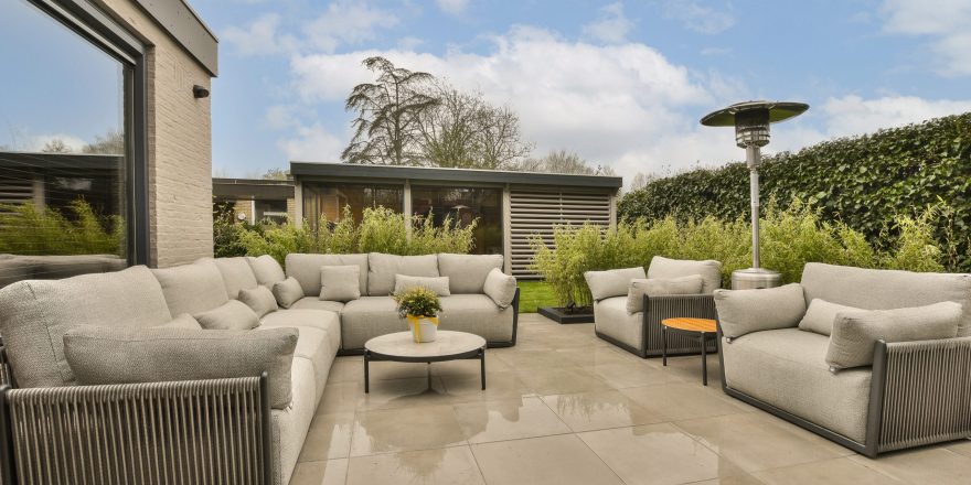 some couches and chairs on a patio with blue skies in the sky behind them are trees, bushes and shrubs