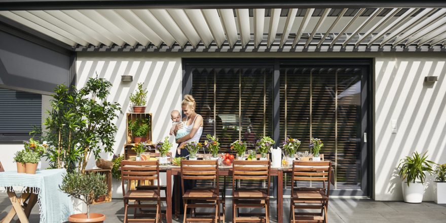 Young woman carrying baby daughter at family lunch by patio table